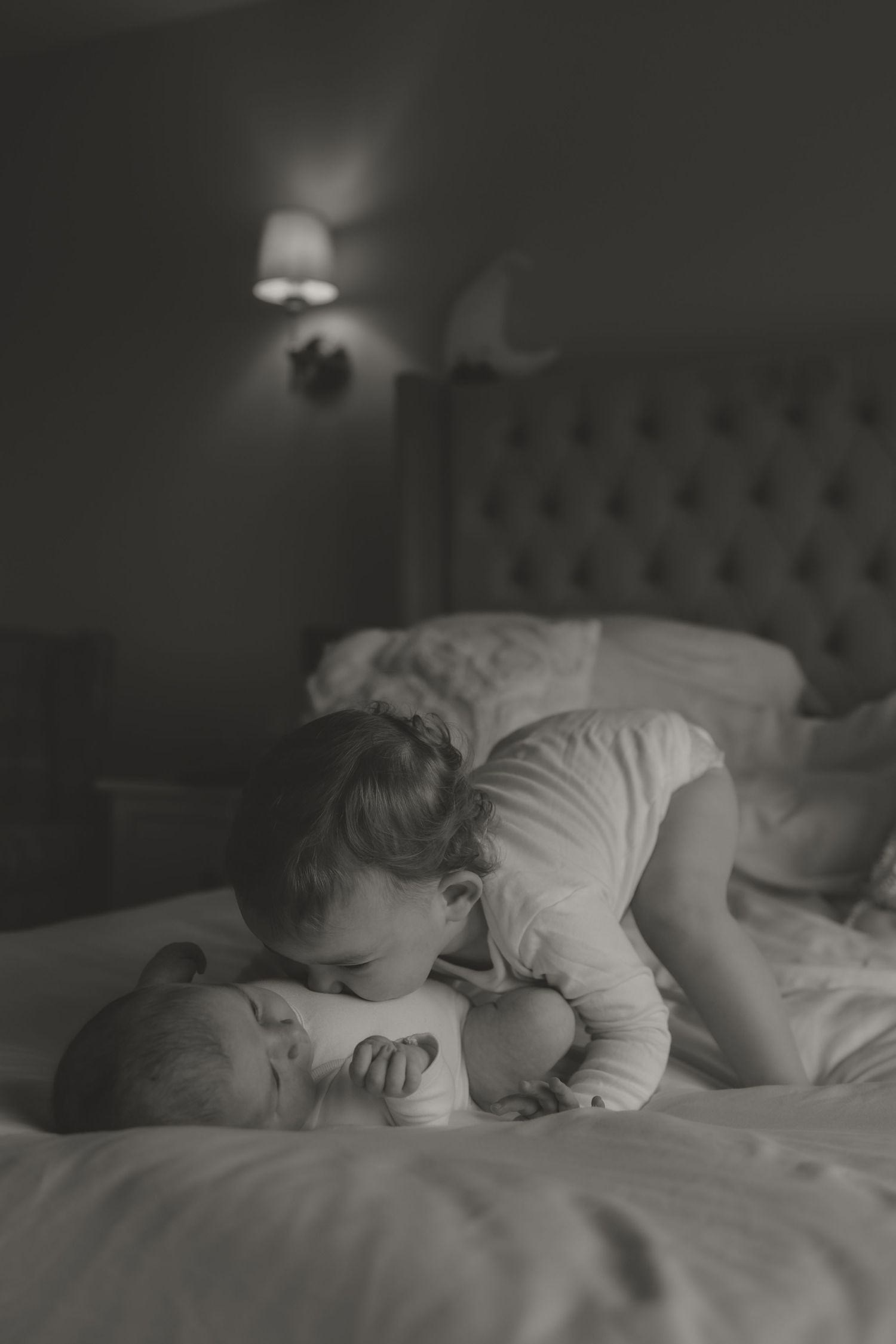 Toddler playfully kissing her new baby sister's tummy, showcase that a small age gap may be chaotic, but oh so beautiful.