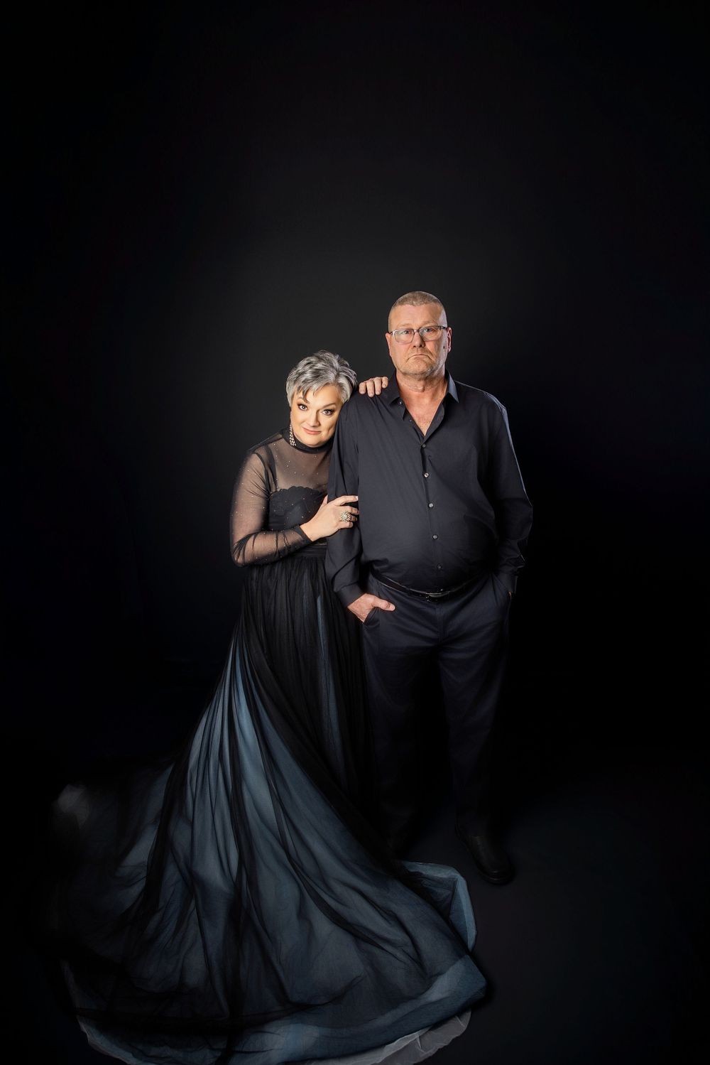 Elegant couple in dark attire pose dramatically in moody studio portraits with black backdrop. Knoxville TN couple photography session.