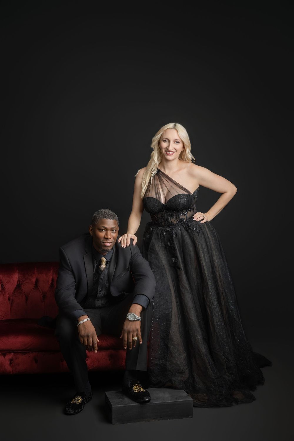 Two people in formal black attire pose together on a black background in a dramatic studio setting. Knoxville TN couple photography session.