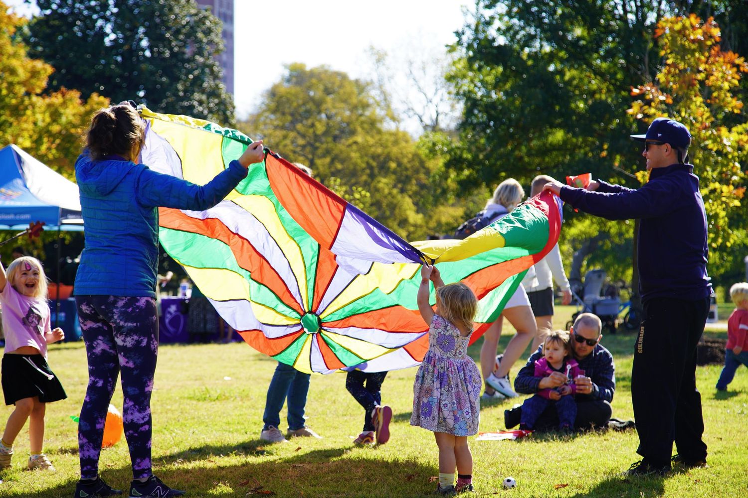 Group activities with colorful parachutes in a sunny outdoor park setting.
