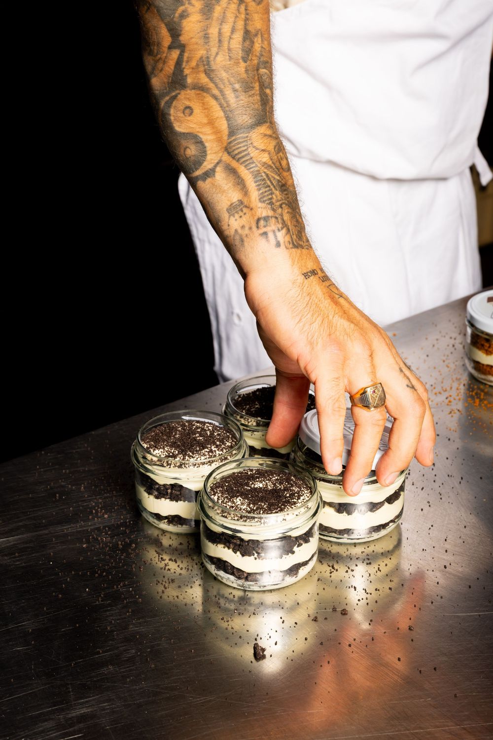 Assembling desserts on a dark surface with tattooed hands placing cream-filled cookie layers.
