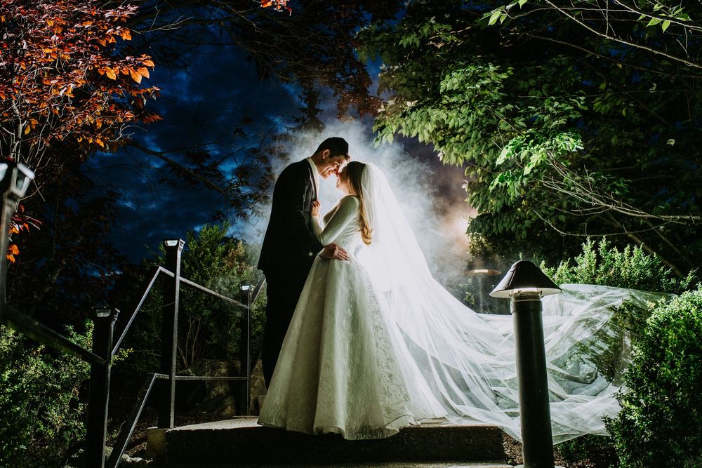 Romantic nighttime wedding portrait illuminated by dramatic backlighting among trees.