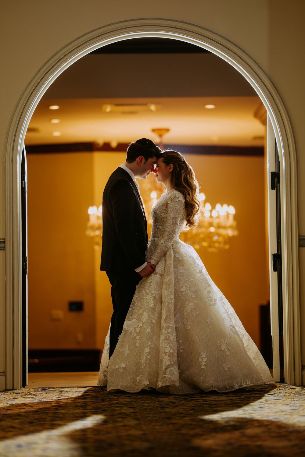 Wedding couple silhouetted through elegant arched doorways with warm lighting.