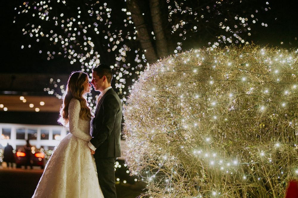 Wedding couple poses beneath sparkling tree lights creating a magical nighttime scene.