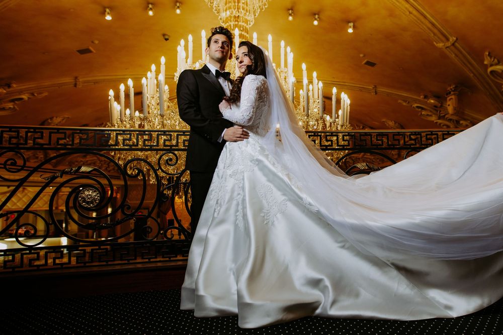 Romantic wedding portrait in an ornate ballroom with glowing candelabras and flowing dress train.