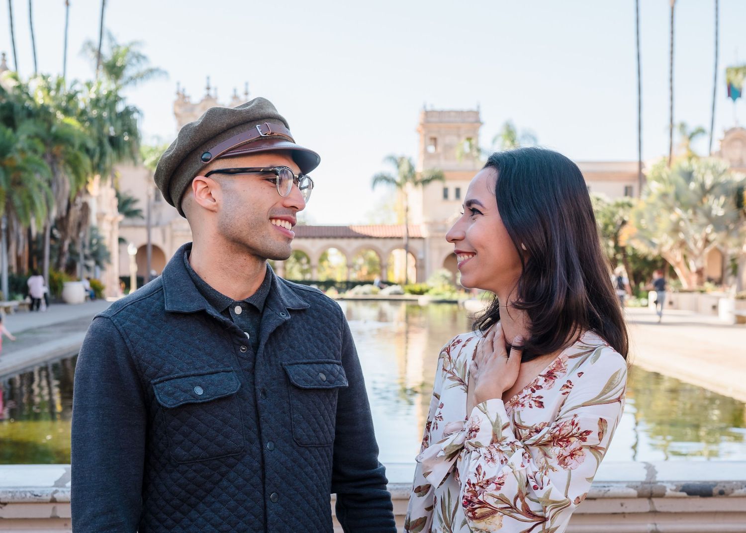 A couple laughs together while walking along a waterfront path on a sunny afternoon.