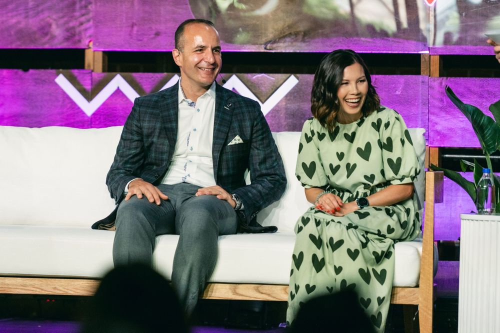 Two people sit together on a wooden bench with purple lighting in the background.