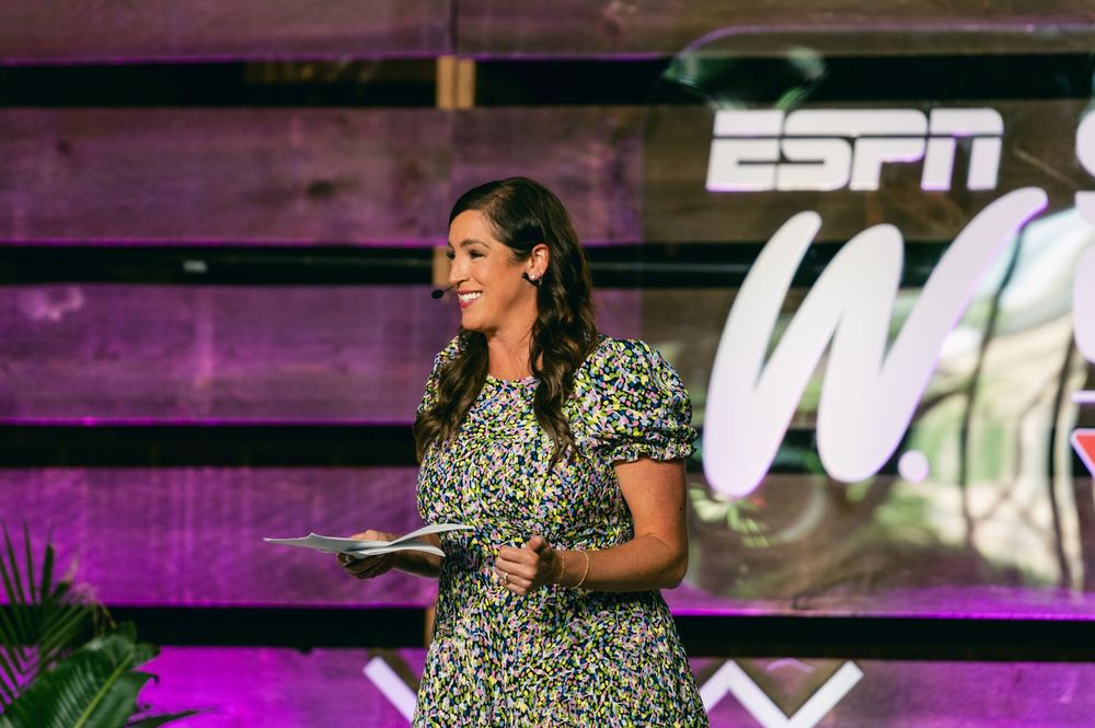 A person in a leopard print top gestures while speaking at an event with colorful lighting and ESPN branding.
