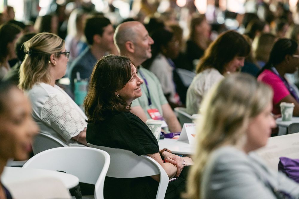 Large audience sitting in rows at a professional conference or seminar with bright lighting.