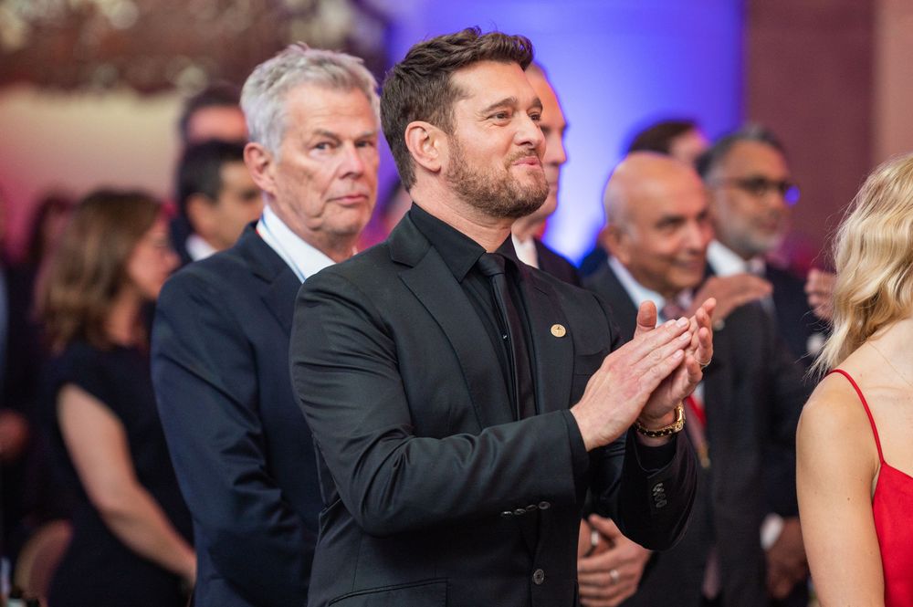 People in formal attire applaud during an event with blue lighting and elegant decor in the background.