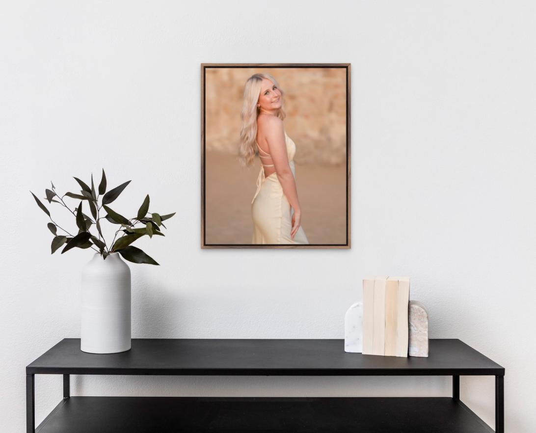 Framed portrait photo of a blonde woman in a backless white dress displayed on a wall above a black console table.
