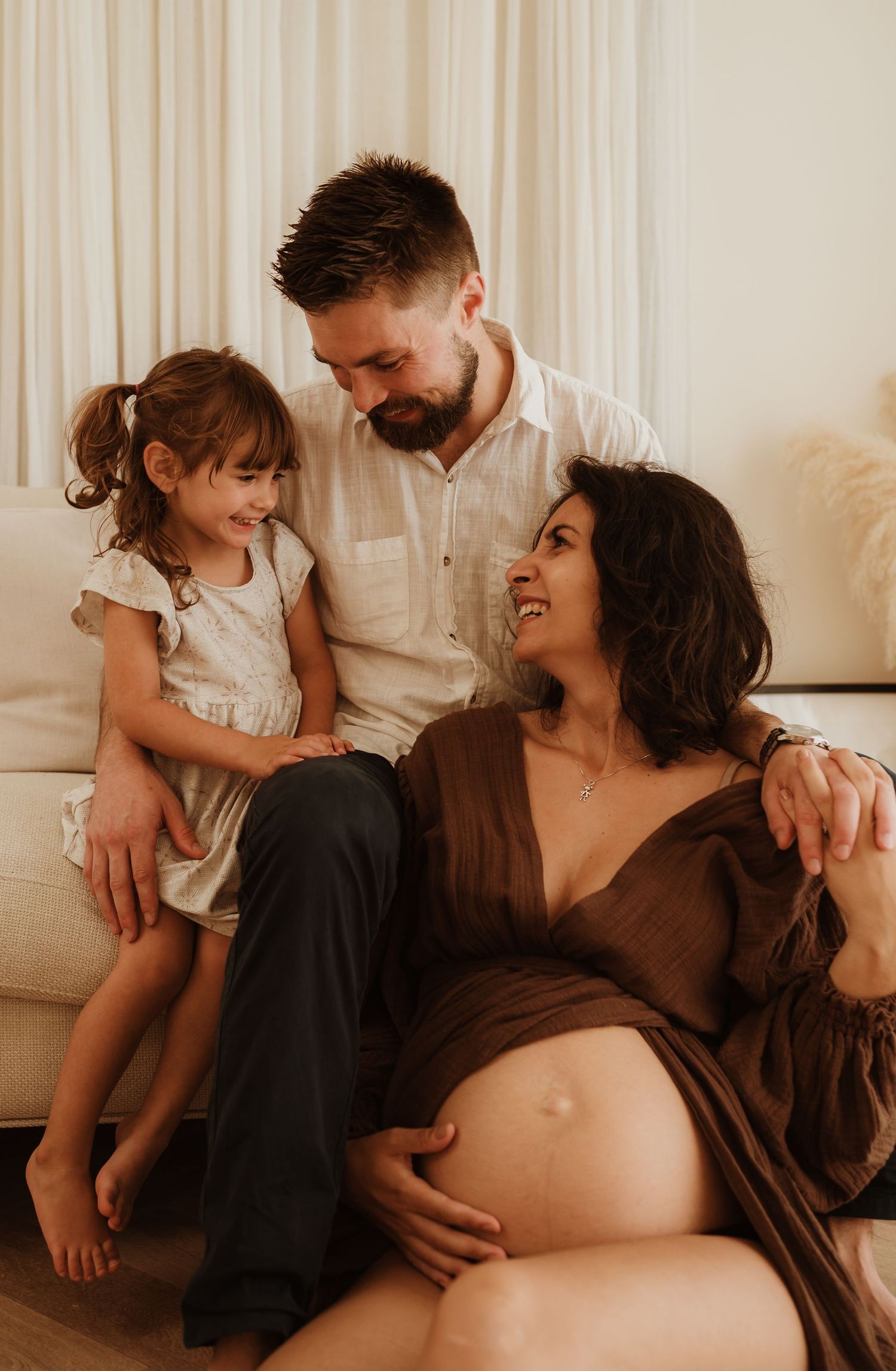 A family shares tender moments together in a series of warm-toned photographs showing a pregnancy photoshoot.