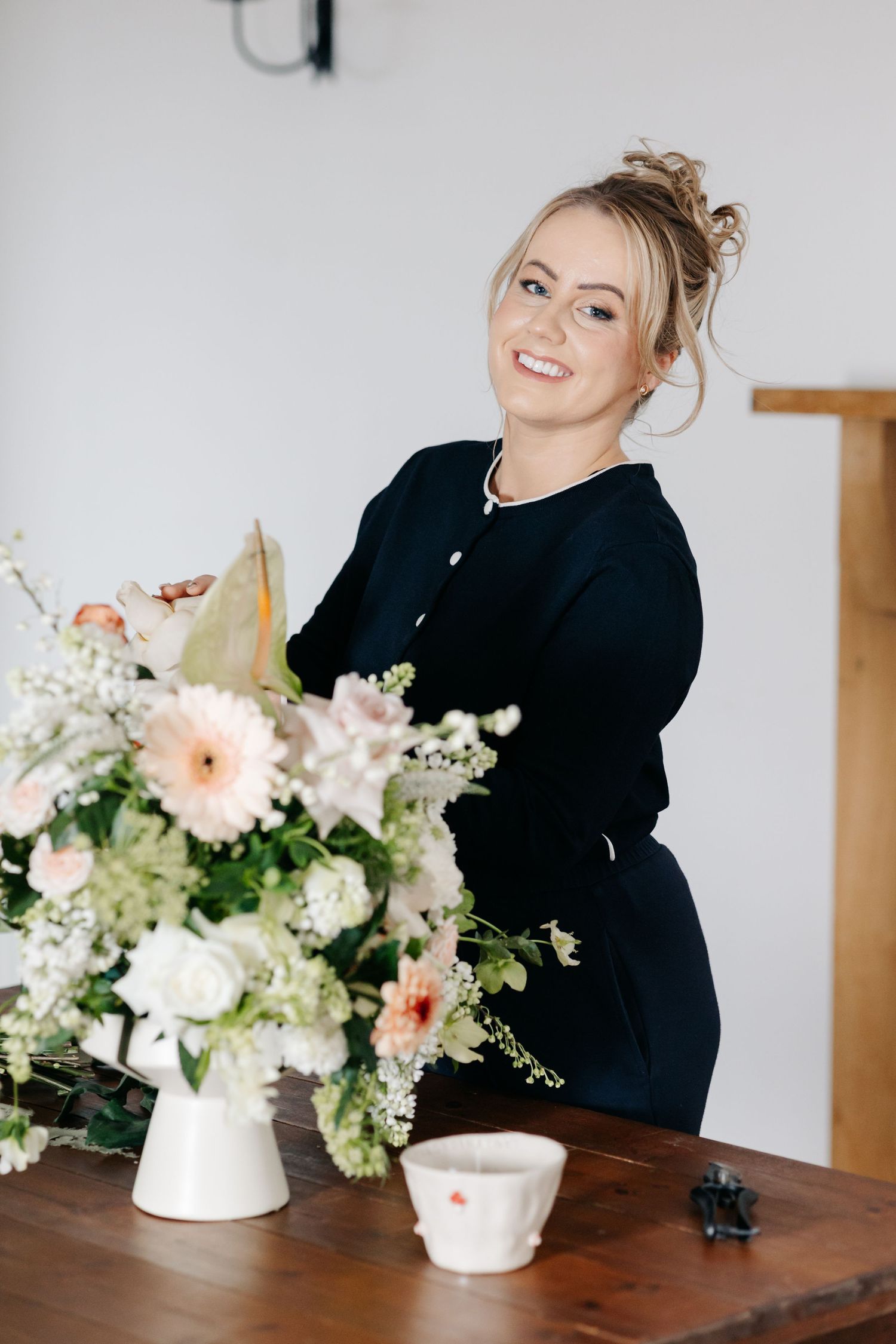 Professional florist in black arranges delicate pink and white floral centerpiece on wooden table at New Forest venue for personal Branding