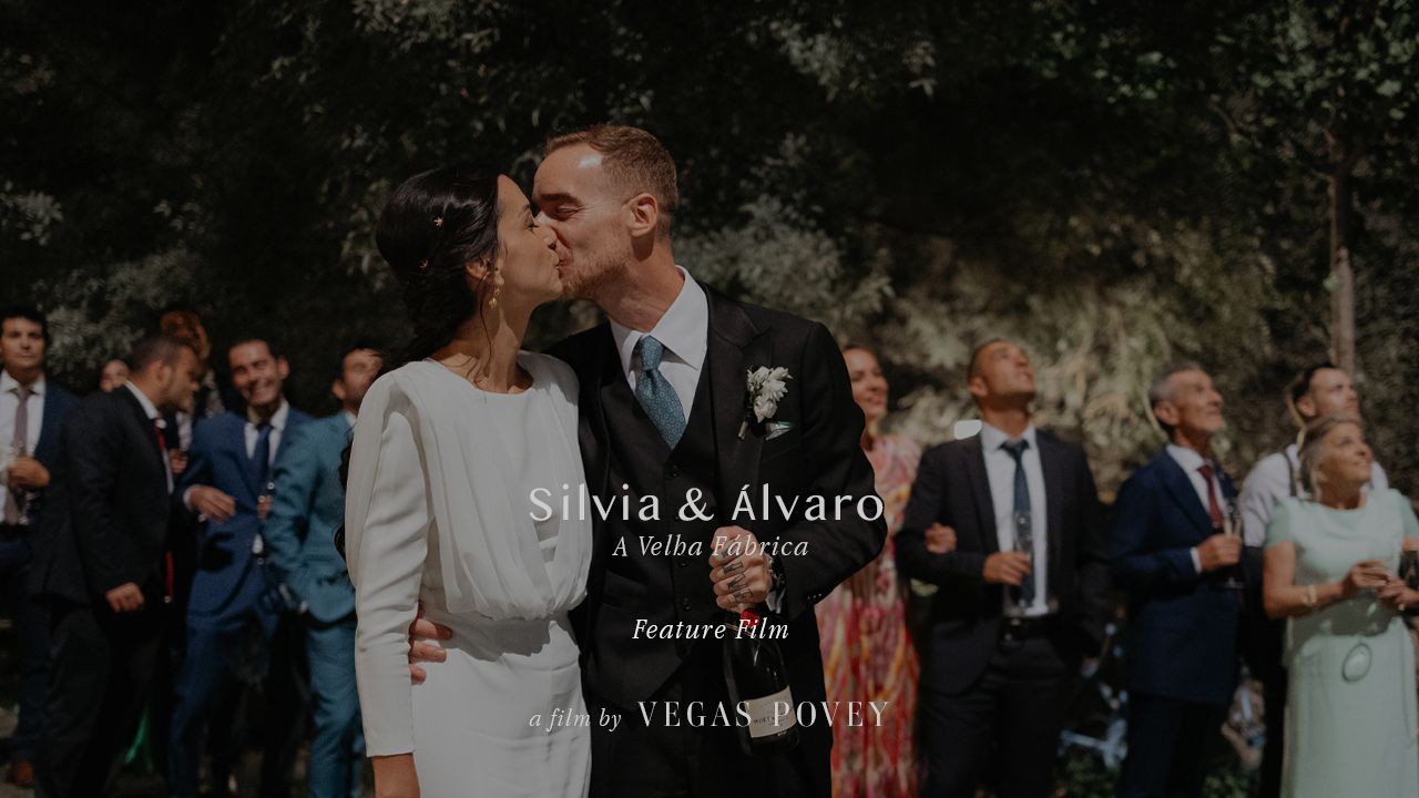 A romantic garden wedding scene with guests gathered in the background during a tender kiss moment.