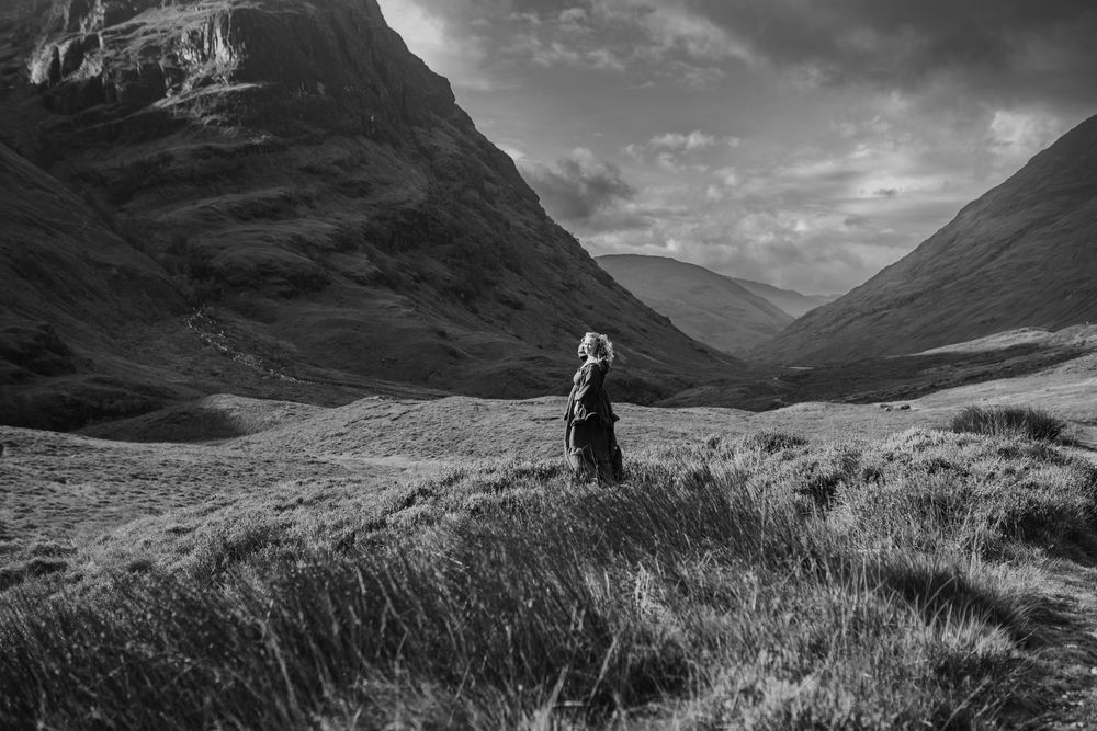 A dramatic black and white landscape photo of the Scottish Highlands with rolling hills and moody clouds.