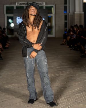 Urban style outfit with distressed gray cargo pants and black jacket presented on runway.
