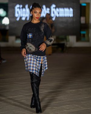 Model walks runway in black sweater and plaid outfit with leather details.