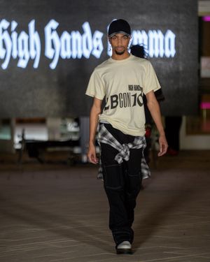 Fashion model walks runway wearing black and white streetwear outfit with baseball cap during fashion show.
