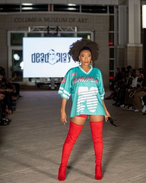Model struts in teal jersey with red thigh-high boots during Columbia Museum fashion show.