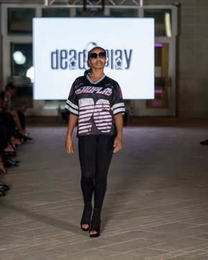 Fashion model struts down catwalk wearing casual black pants and graphic t-shirt ensemble.
