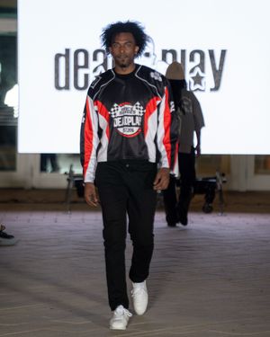 Model presents sporty black and red striped outfit with white sneakers on runway.