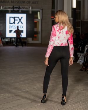 Fashion model in pink tie-dye top and black leggings walks runway at DFX fashion show.