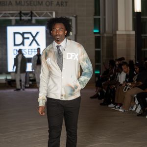 Model showcases formal white shirt and black pants combination on fashion runway.