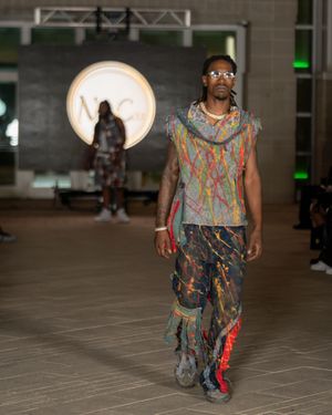 Model walks runway in colorful abstract print outfit at fashion show.