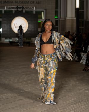 Runway model wearing metallic patchwork dress with flowing fabric details performs at fashion show.