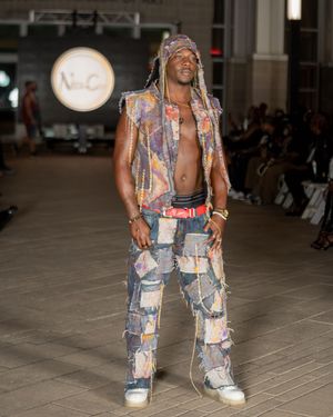 Distressed denim patchwork ensemble with matching vest showcased on indoor fashion runway.