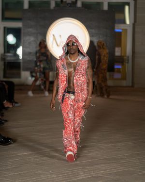 Fashion model walks runway in sparkly pink sequined jumpsuit and white sneakers at fashion show.