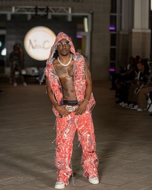 Model showcases coral lace jumpsuit with matching vest during fashion show runway presentation.