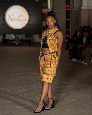 Fashion model showcases colorful printed shorts ensemble on dark runway.