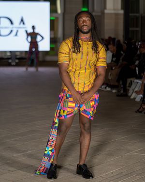 Fashion model walks runway in yellow t-shirt and colorful patterned shorts at Columbia Museum of Art fashion show.