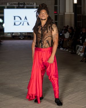 Model presents flowing red satin ensemble with black lace detail at fashion event.