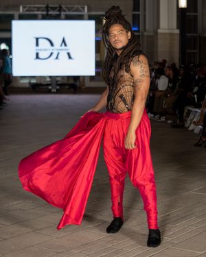 Fashion model wearing a flowing red silk outfit with black boots walks the runway at a fashion show.