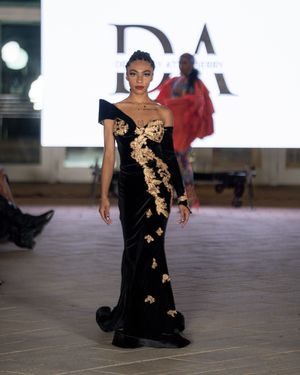 Elegant black evening gown with gold floral embellishments displayed on fashion runway.