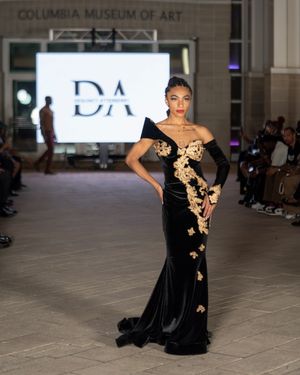Model presents elegant black gown with gold floral appliques on runway.