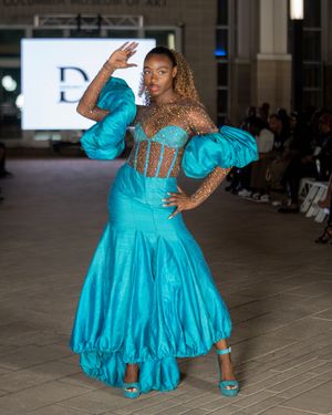 Turquoise ballgown with dramatic ruffled skirt displayed during fashion show performance.