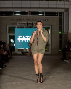 Olive green military-inspired outfit with black boots presented on fashion runway.