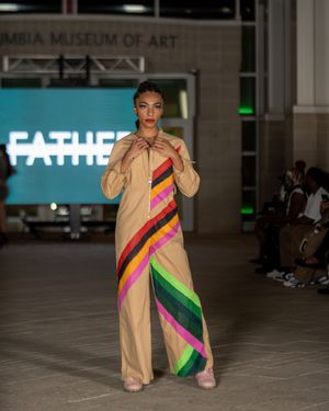 Model showcases tan outfit with colorful geometric stripe design on fashion runway.