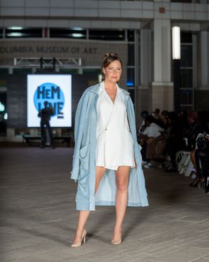 Model presents casual chic look with light blue jacket and white top on fashion runway.