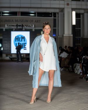 Runway model wearing light denim jacket over white shirt with nude heels at fashion show.