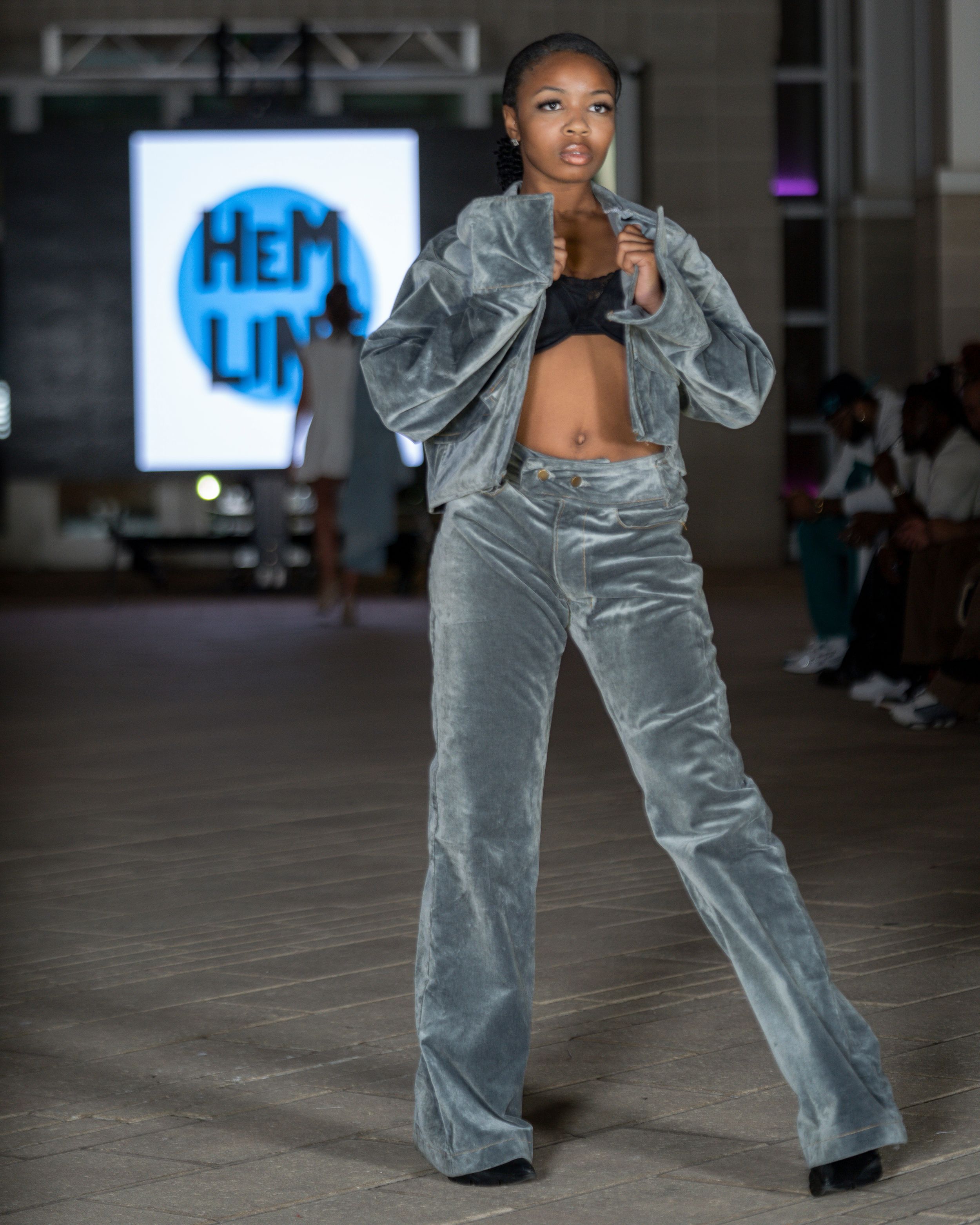 Model showcasing silver velvet wide-leg pants on an indoor runway with studio lighting.