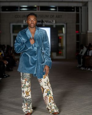 Model showcases blue denim jacket with printed pants during fashion show.