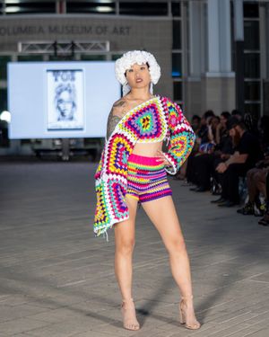 Model walks runway in vibrant rainbow crochet dress with dramatic puff sleeves at Columbia Museum of Art fashion show.