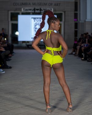 Fashion model showcases neon yellow swimwear design on museum runway.