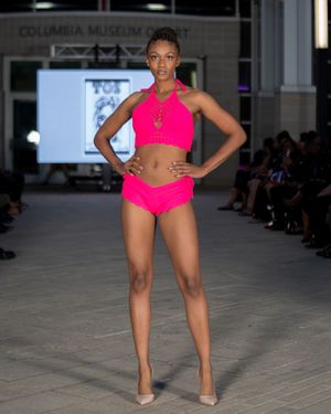 A model walks the runway in a hot pink swimwear set during a fashion show presentation.