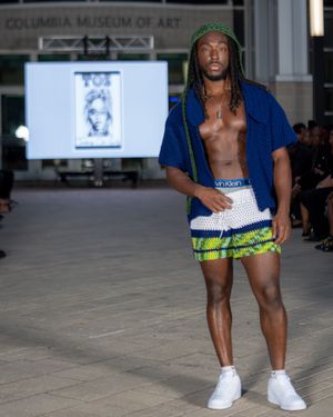 Models walk the runway wearing white crochet shorts with neon accents during a fashion show presentation.