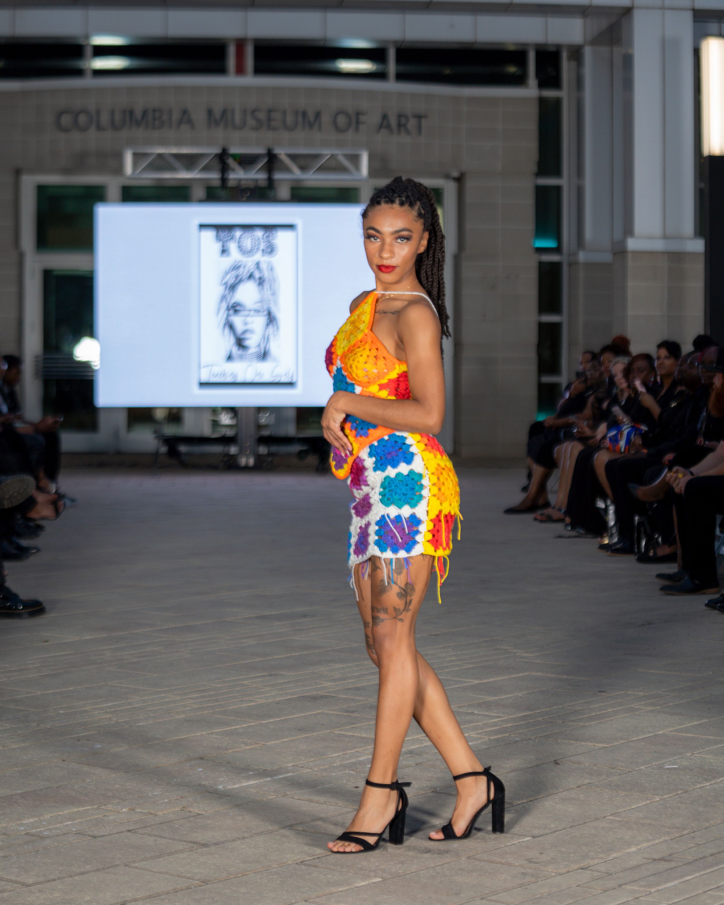 Fashion model walks runway in colorful floral swimwear and black heels at Columbia Museum of Art fashion show.